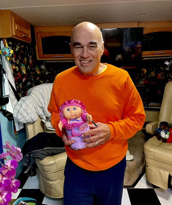 Steve in an orange sweater holding a tiny Cabbage Patch baby