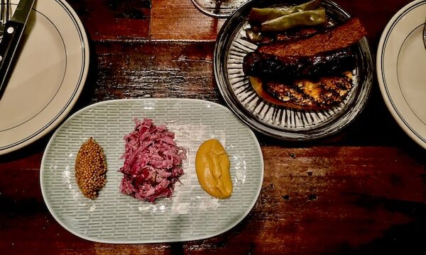 Oval plate with condiments next to round plate with sausage on a toasted bun and pickles at Five and Ten Athens GA