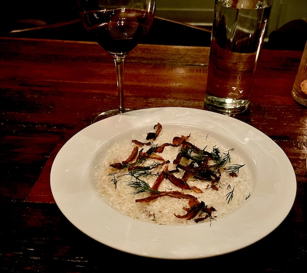 Mushroom risotto in a white shallow bowl on a wood table at Five and Ten Athens GA