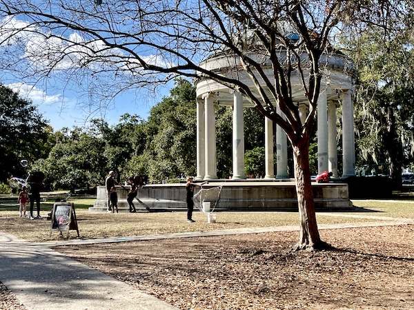 Boy blowing bubbles by a pillared gazebo in front of Café du Monde City Park NOLA