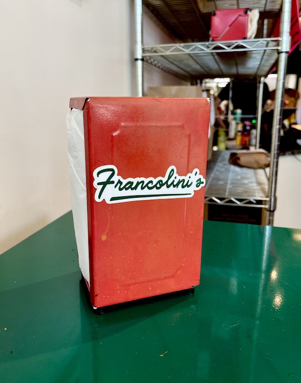Francolini's Italian Deli NOLA a dark green high top table with a red napkin dispenser branded with the name.