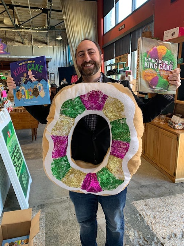 Man with beard holding a large donut shaped pillow in purple, green and gold at SoFab NOLA is So Fabulous!
