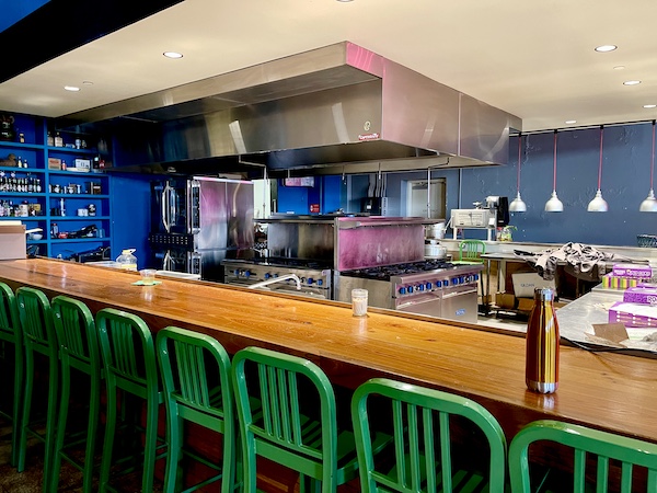 Bar with green bar stools and kitchen equipment in center at SoFab NOLA is So Fabulous!
