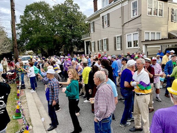 Lots of people in Mardi Gras colors in the street listening to a band at the 52 Year Mardi Gras Tradition