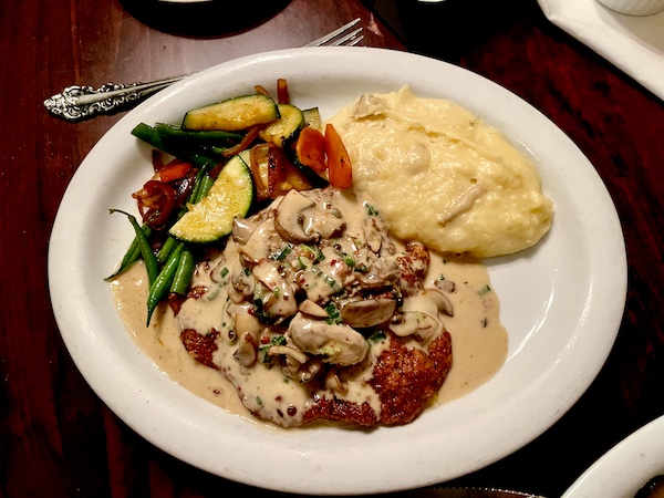 White plate topped with mashed potatoes, mixed vegetables and veal with sauce put us in a Mardi Gras State of Mind