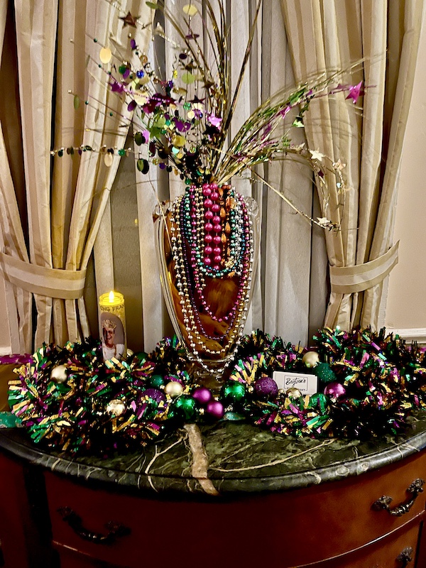 Mardi Gras State of Mind is a vase and table draped in colorful Mardi Gras beads