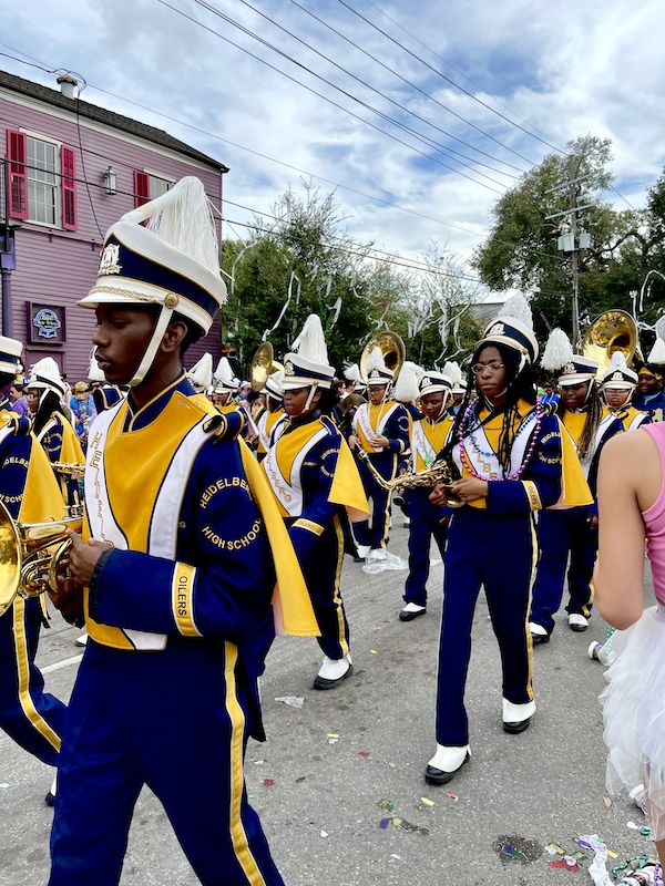 High school marching band in dark purple and gold uniforms at Our First Mardi Gras Parade