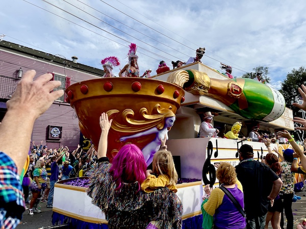 Costumed people in Our First Mardi Gras Parade on a float with a huge bottle of champagne being poured into a large gold chalice
