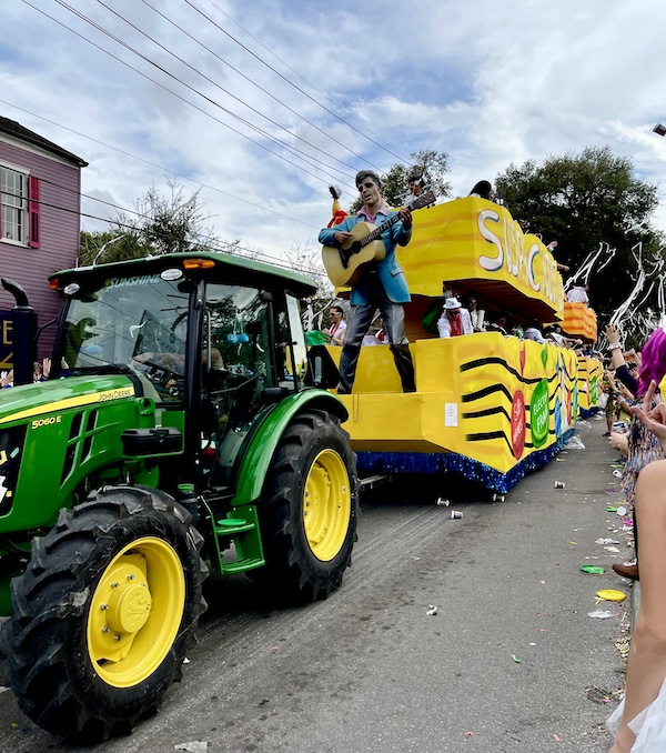 Yellow float with statue of Elvis on front is being pulled by a green tractor at Our First Mardi Gras Parade