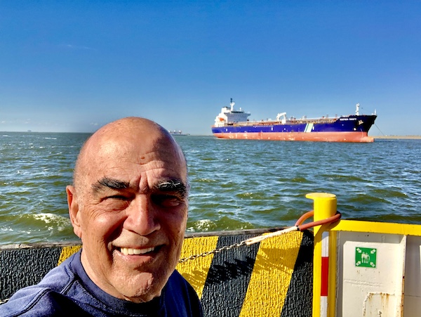 Steve at the bow of our ferry with a blue and red freighter behind him.