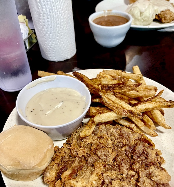 Our First Taste of Chicken Fried Steak on a plate with french fries, gravy and a roll.