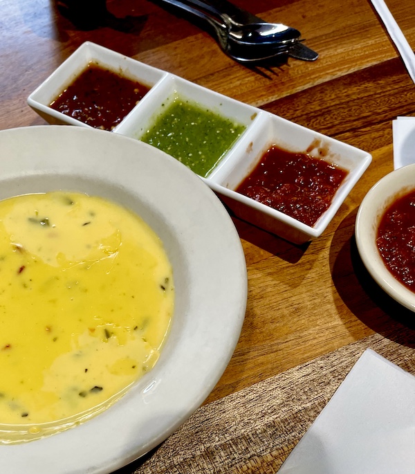 Bowl of cheese dip and triple dish of 3 salsas on a wood table at Abuelo's Mexican Restaurant Midland TX