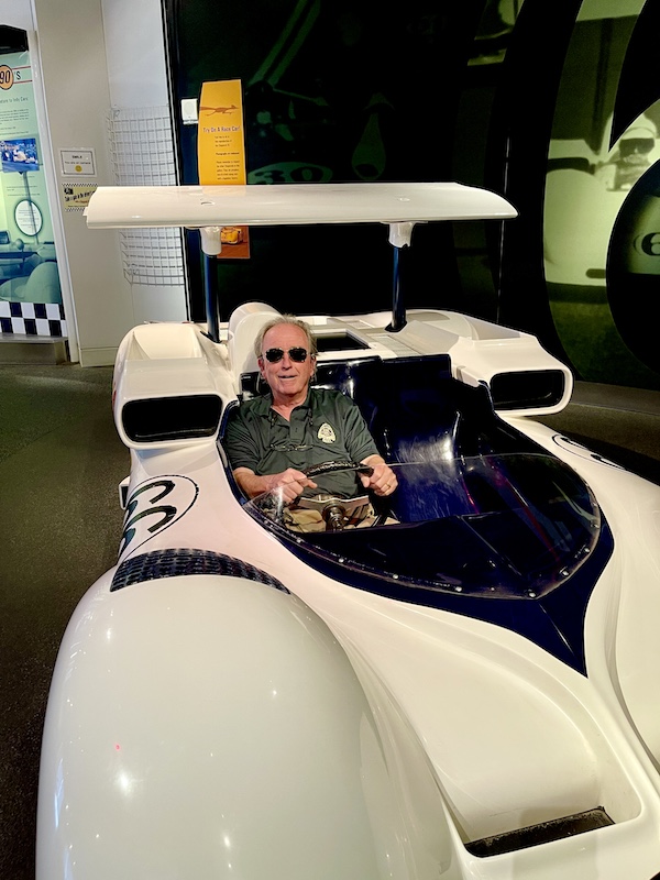 Mack with aviator glasses behind the wheel of a white racing car at the Chaparral Gallery Petroleum Museum
