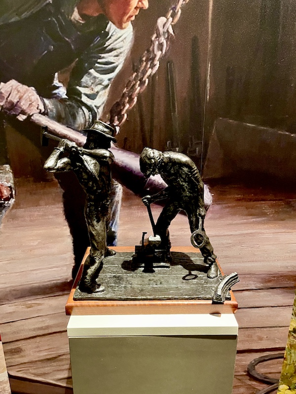Painting by Tom Lovell capturing Permian Basin life in background behind bronze sculpture of men working the oil fields at the Petroleum Museum Midland Texas
