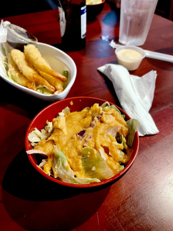 Red bowl filled with salad and an orange dressing in foreground. In background is a bowl of tempura shrimp, all from Sakura Sushi Sulphur Springs TX