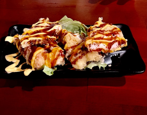 Black plate topped with shrimp and crab rolls with 3 sauced drizzled on top at Sakura Sushi Sulphur Springs TX
