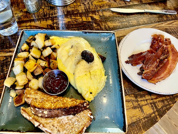 Square blue plate topped with an omelet, home fries, toast, jam and a white plate with bacon at First Watch Tucson Arizona