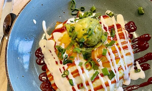 Round blue plate topped with eggs, chorizo a grid pattern of white sauce and a scoop of smashed avocado at First Watch Tucson Arizona