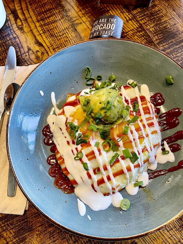 Round blue plate topped with eggs, chorizo a grid pattern of white sauce and a scoop of smashed avocado at First Watch Tucson Arizona