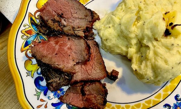 Garlic Horseradish Mashed Potatoes topped with a pat of melting butter sit next to sliced steak on a plate with a yellow and blue rim.