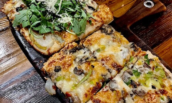 Rectangular slices of pizza on a plate sitting on a dark wood table at Locale Neighborhood Italian Tucson