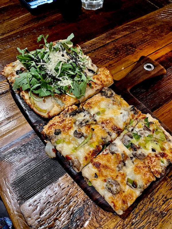 Rectangular slices of pizza on a plate sitting on a dark wood table at Locale Neighborhood Italian Tucson