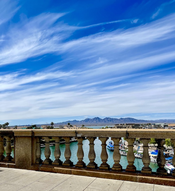 View of mountains and London Bridge Lake Havasu AZ guard rails along with deep blue sky and streaky white clouds.