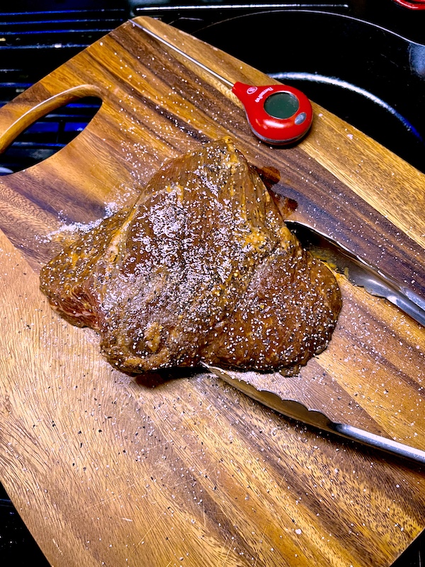 Marinated San Diego Style Grilled Tri-Tip ready to grill and sitting on a wood cutting board with tongs