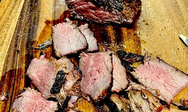Sliced San Diego Style Grilled Tri-Tip cooked medium rare and sitting on a wood cutting board
