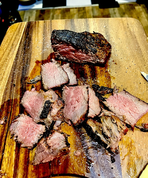 Sliced San Diego Style Grilled Tri-Tip cooked medium rare and sitting on a wood cutting board