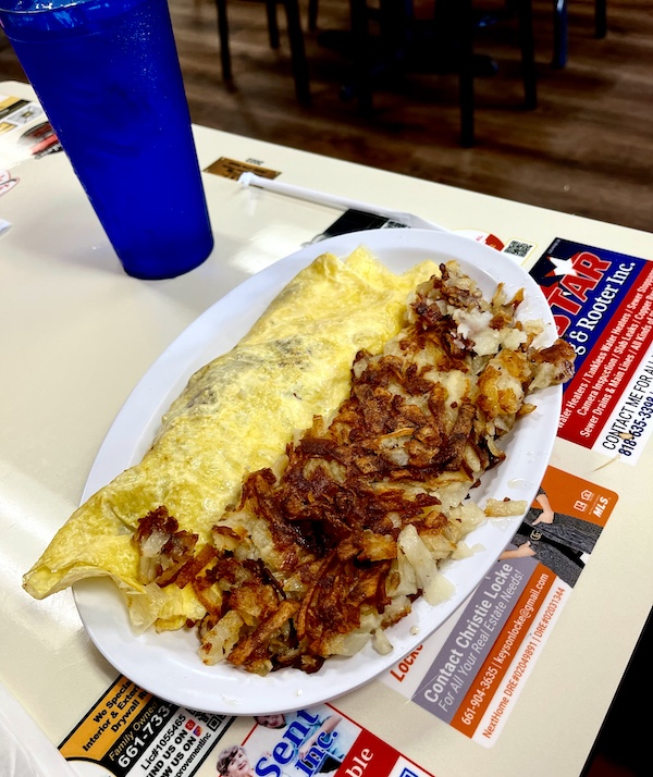 Oval white plate topped with an omelet and hash browned potatoes for Brunch at Crazy Otto's Diner