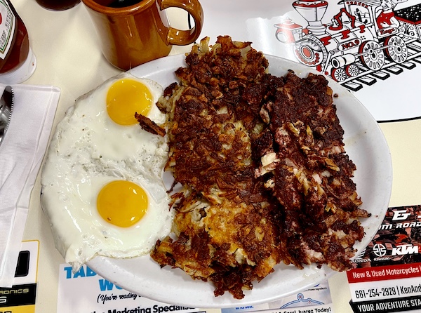 Round white plate topped with 2 sunnyside up eggs, corned beef hash and hash browns for my Brunch at Crazy Otto's Diner