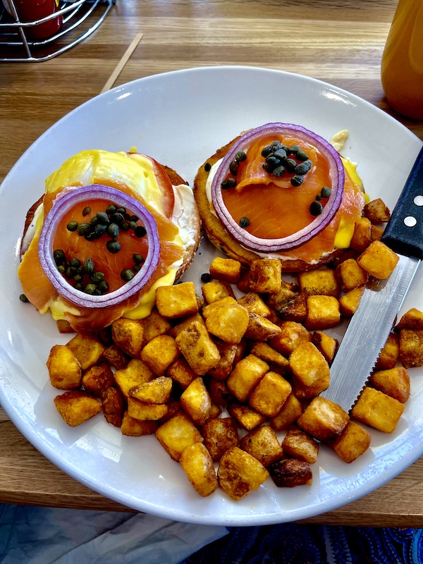 White plate topped with 2 eggs benedict with lox and home fries for Brunch at Scrambled Henderson NV