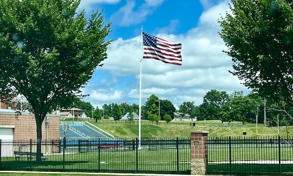 Happy July 4th 2024! with a flag, football field and trees.
