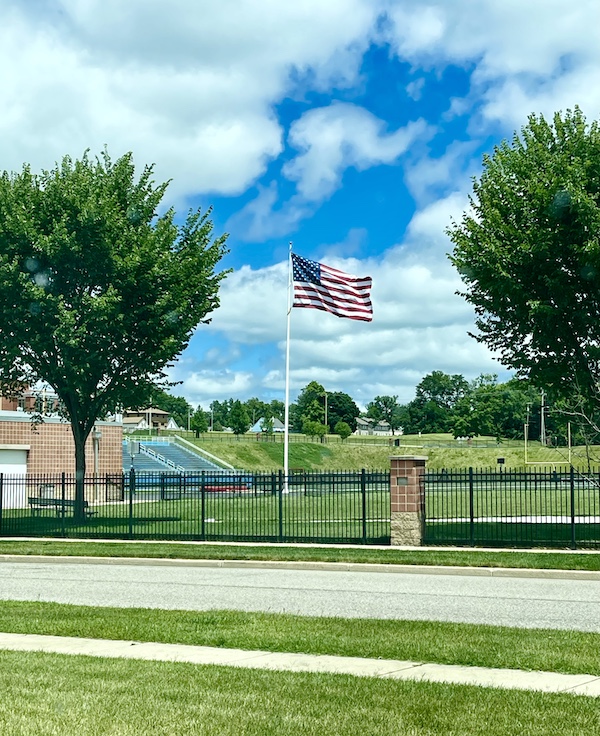 Happy July 4th 2024! with a flag, football field and trees.