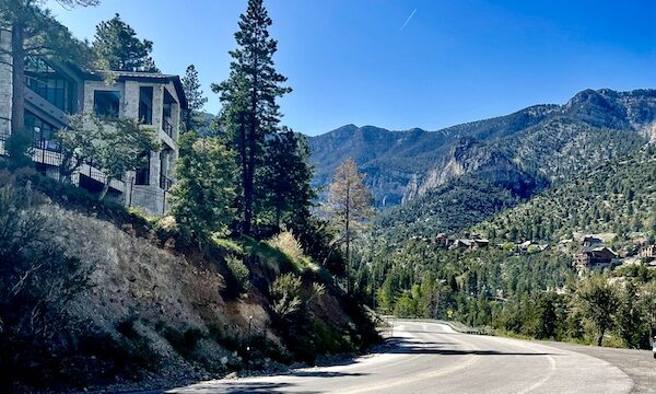 The back of a stone house in Scenic Mount Charleston Nevada with trees, mountains and paved road.