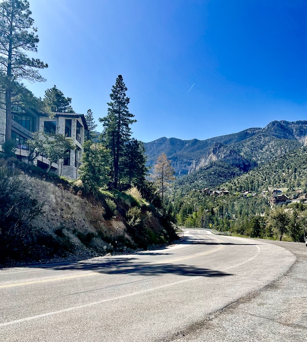 The back of a stone house in Scenic Mount Charleston Nevada with trees, mountains and paved road.
