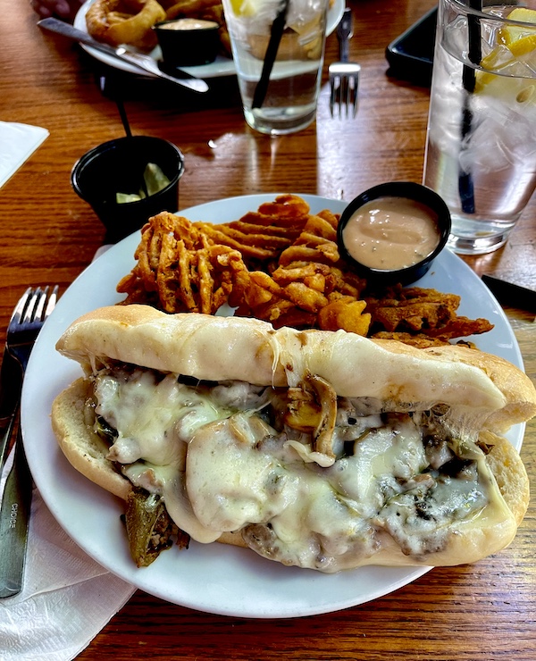 White plate topped with a very stuffed Philly Cheesesteak with waffle fries for lunch during our day at Scenic Mount Charleston Nevada