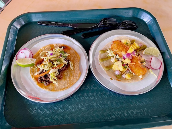 Dark teal cafeteria tray topped with 2 tacos from Trejo's Tacos Hecho en Los Angeles