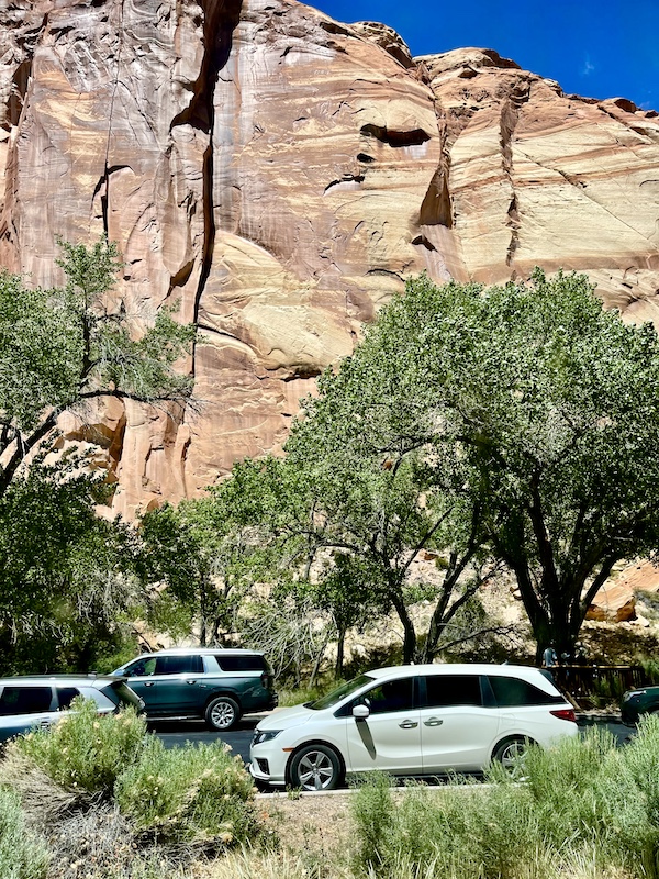 Pink and white marble patterned rock formation with cars and trees in foreground at Capitol Reef National Park