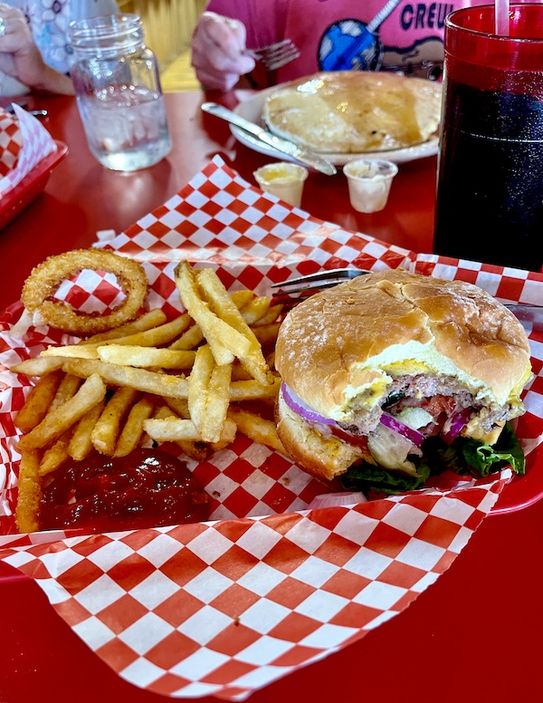 Red basket with red and white checkered paper topped with a cheeseburger, fries, 1 onion ring and ketchup for lunch in Delightful Parowań Utah