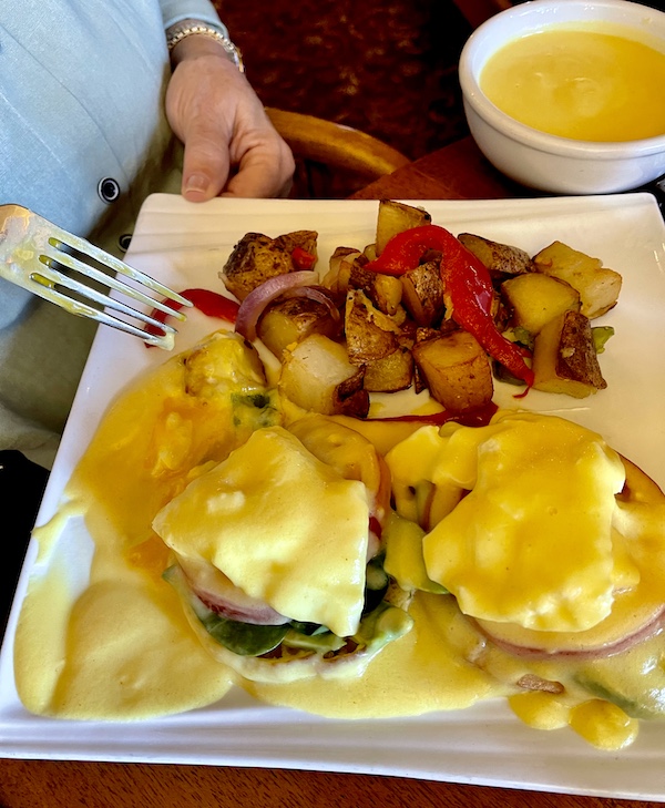 White square plate topped with poached eggs on English muffin halves with creamy sauce and home fries at Diamond Belle Saloon Durango
