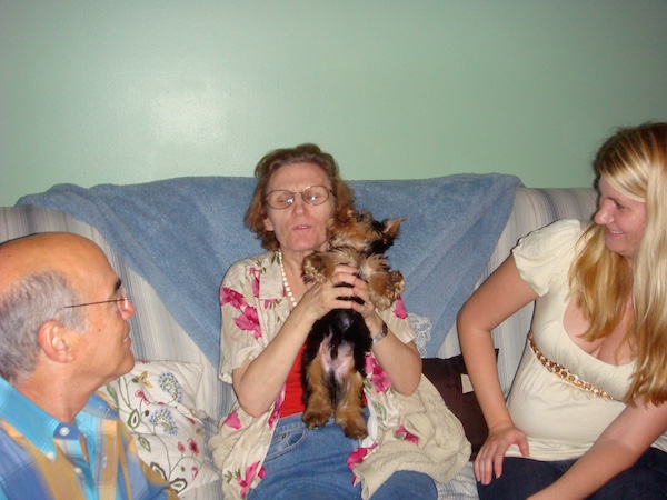 Our Hershi as a puppy sitting on a gray sofa with 3 people.