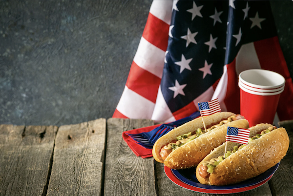 Wood picnic table, American flag and a pair of hotdogs in buns to celebrate Happy Labor Day 2024