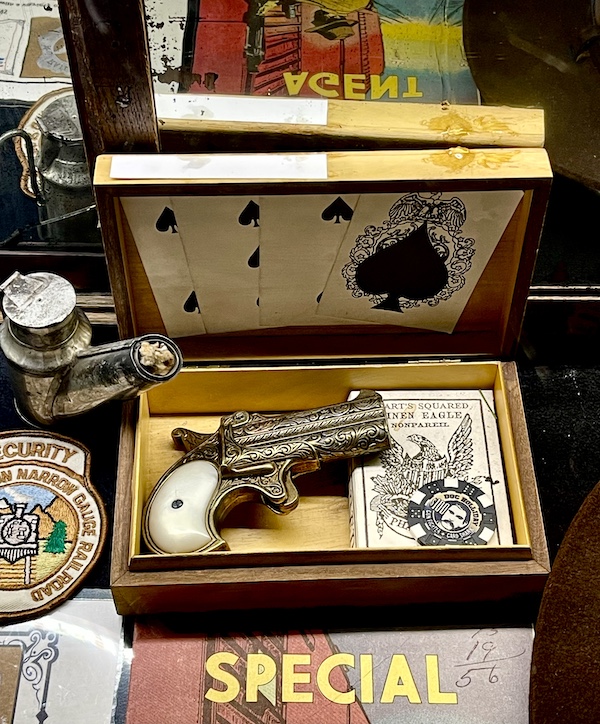 Petite handgun with carving and ivory handle in a wood display box.