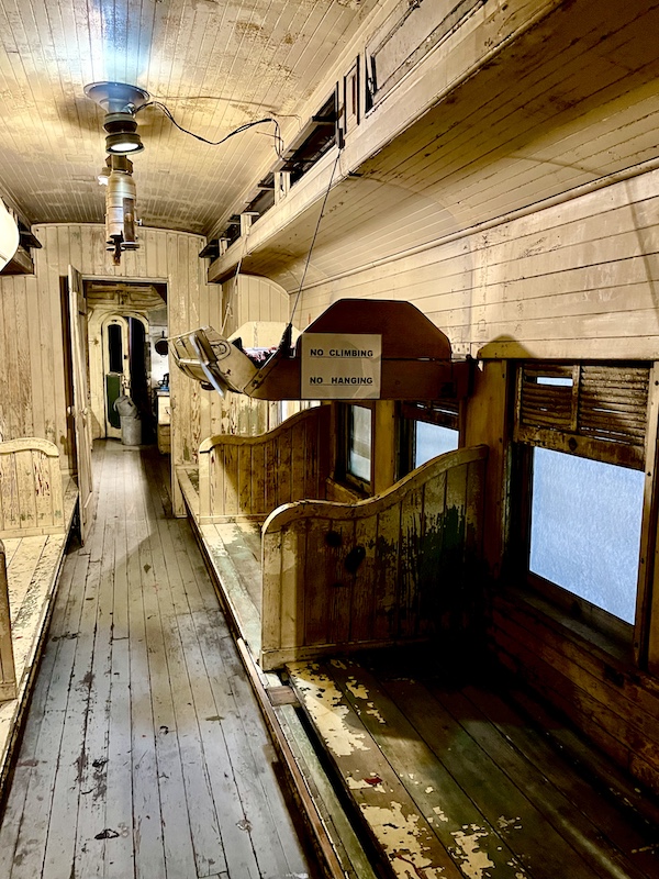 Light wood interior of a sleeping car showing a bed hanging from chains