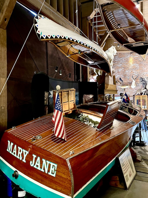 Canoes hang from ceiling and wood speedboat on floor.