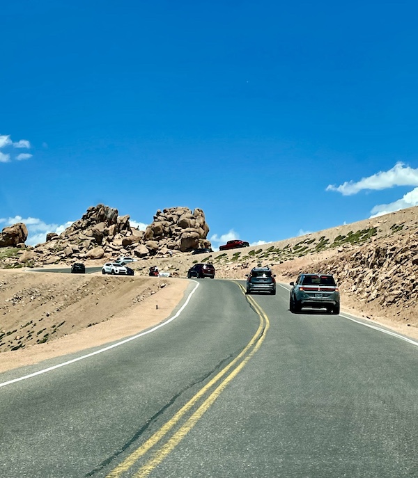 Cars on a rock lined highway that goes back and forth up Pikes Peak in Colorado