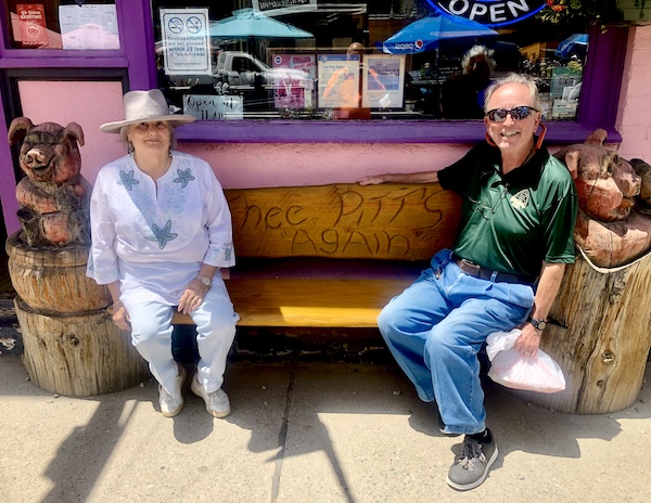 Man and woman on a wood bench in front of Thee Pitts Again BBQ