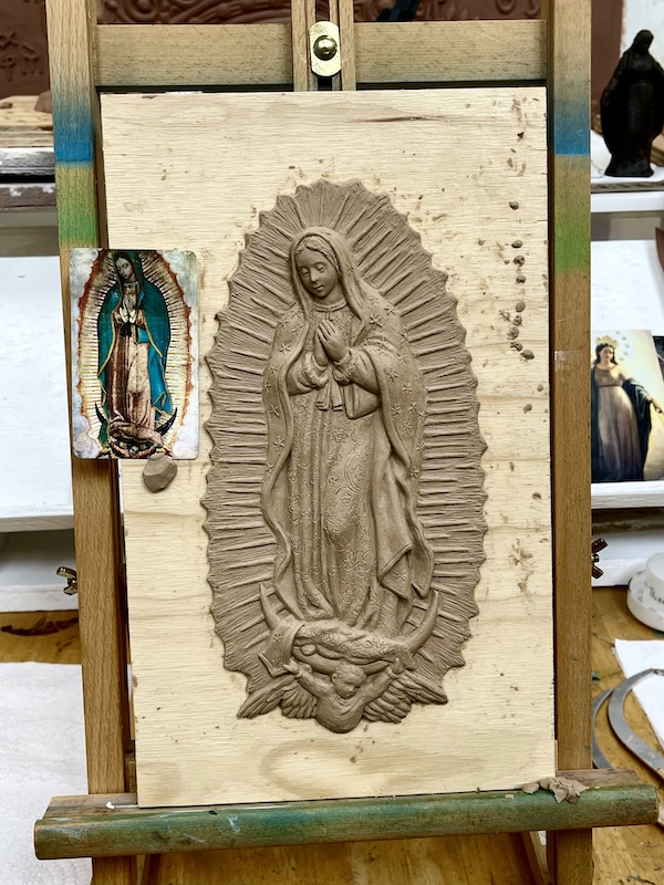 Clay sculpture on an easel with color photo of what's being created clipped to side.